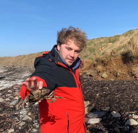 A student on a pebble beach holding a crab