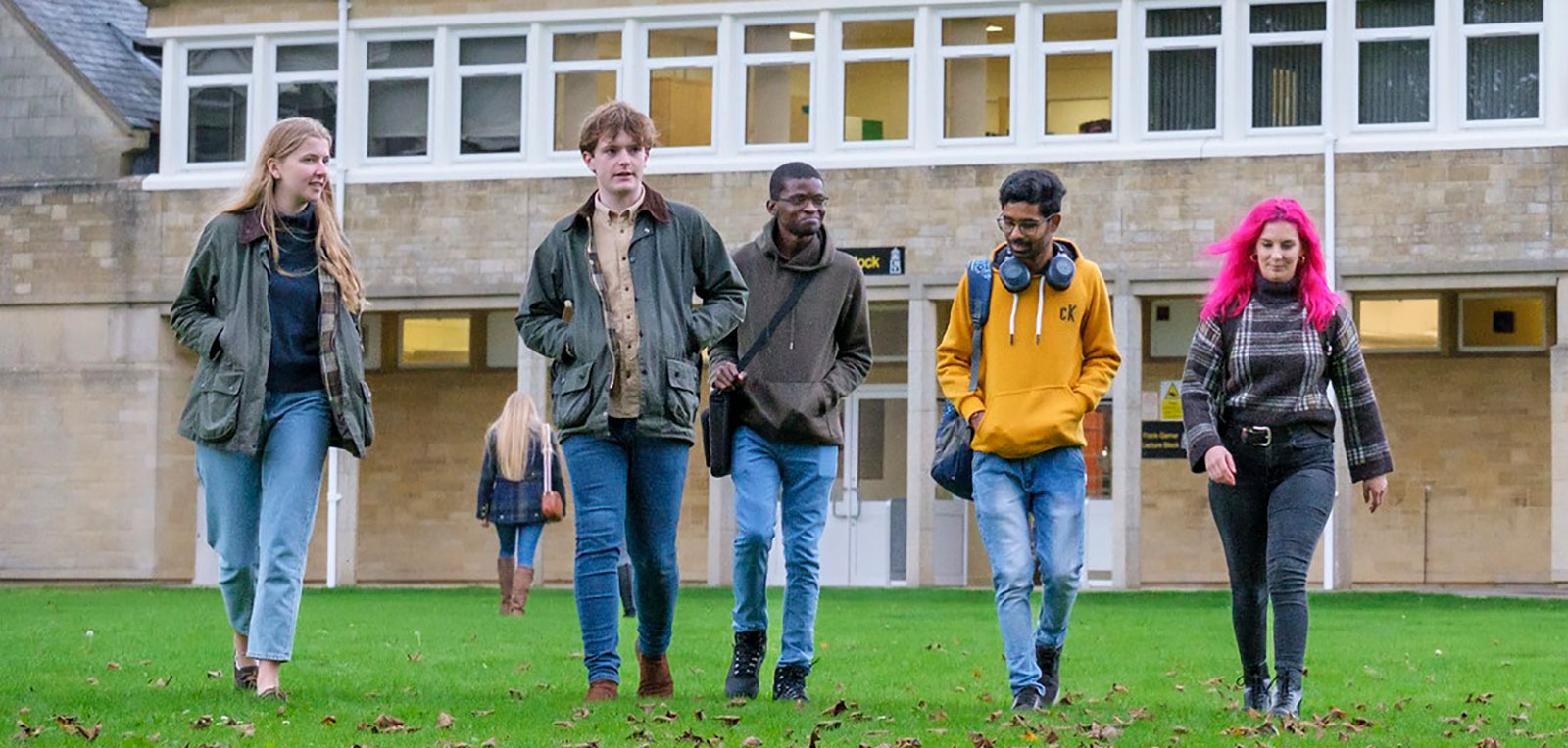 five students walking across the grass quad on campus