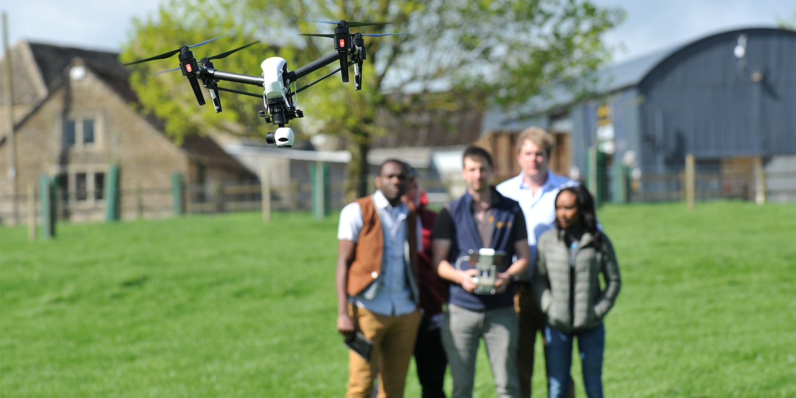 A group of four people in a field, one of whom is flying a drone