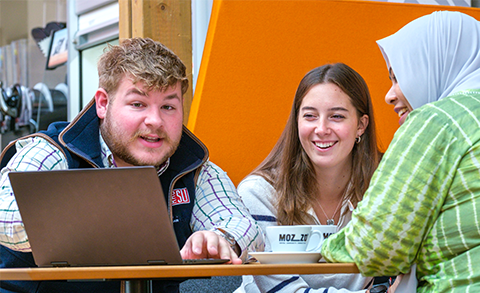 Three students sat in a cafe looking at a laptop