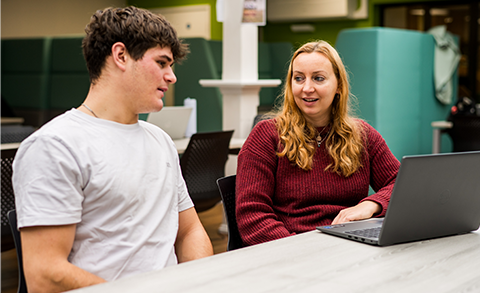 Student and member of staff sat at table with laptop