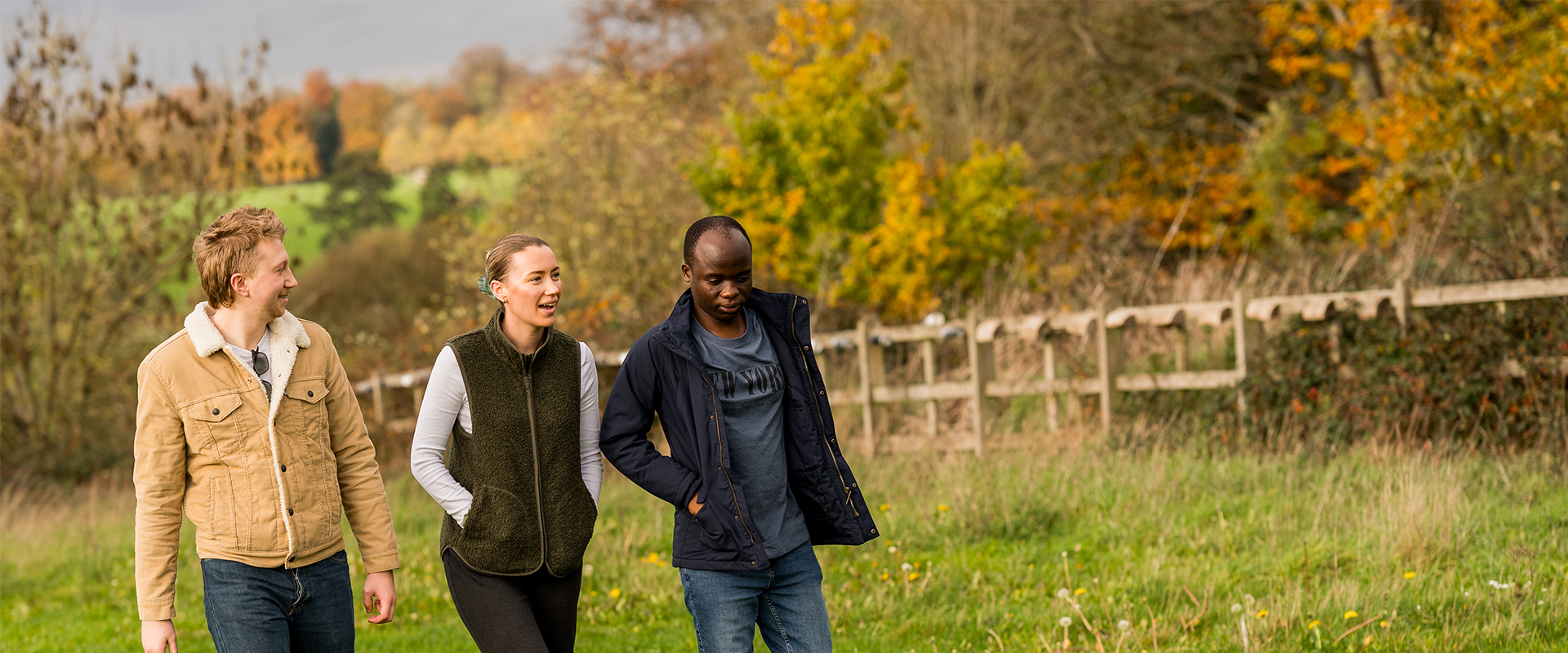 three students walking through a green field