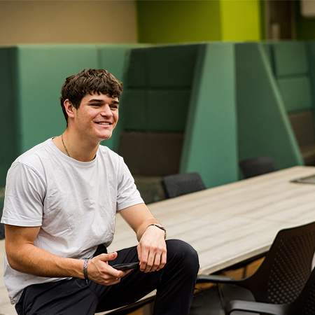 A student sat on a table with a mobile phone in his hand, smiling