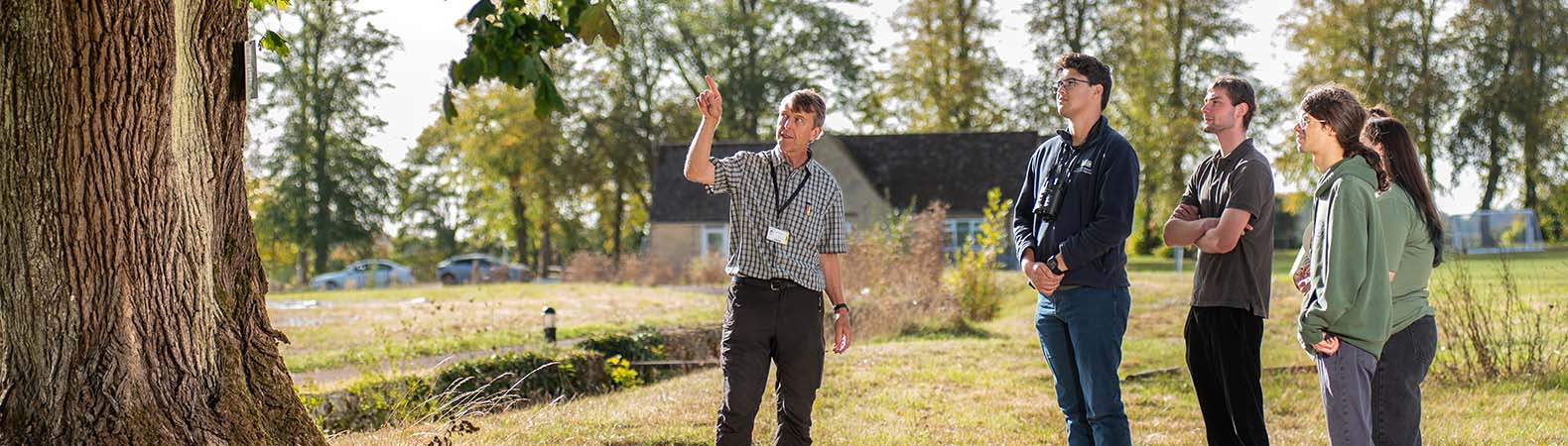 A lecturer talking to a group of students and pointing to a tree