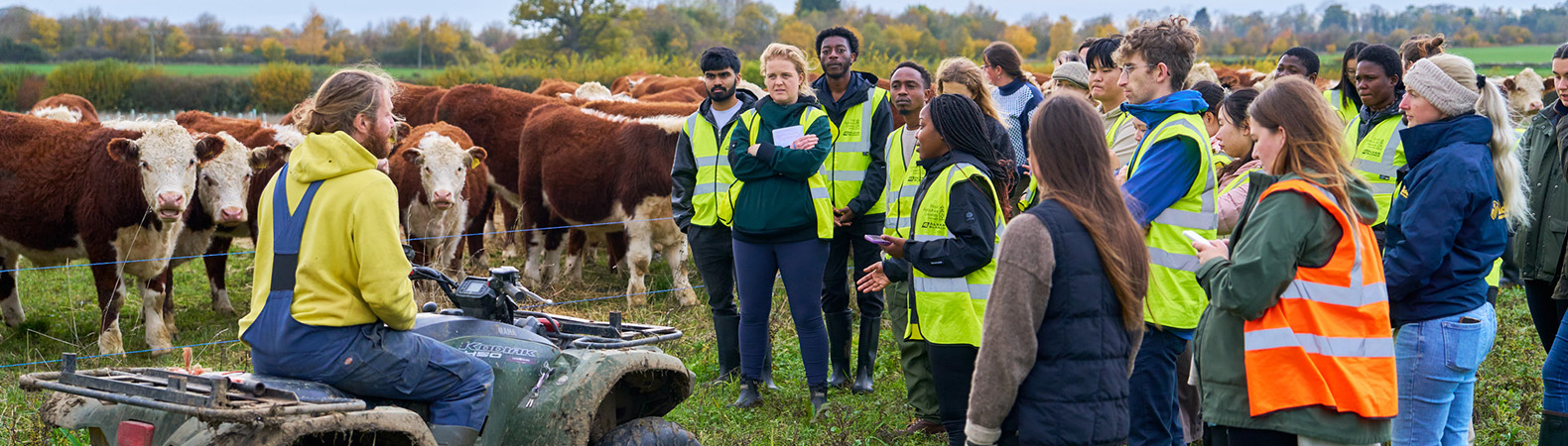 lecturere on quad bike with cows in background and students gathered around in high vis jackets