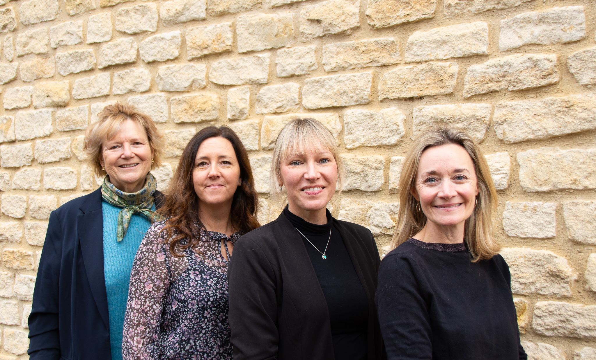 Four people standing in front of Cotswold stone wall