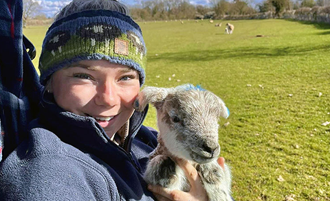 Maisie holding a lamb in a field