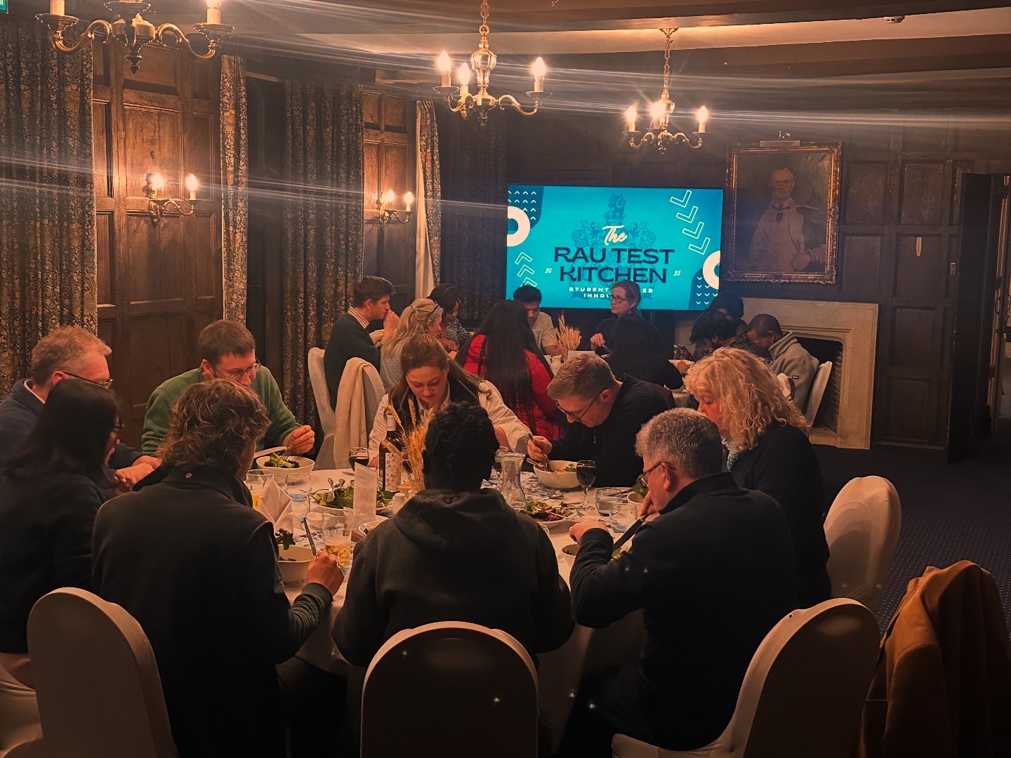 Staff and students sat in dining room around a table eating at the RAU test kitchen