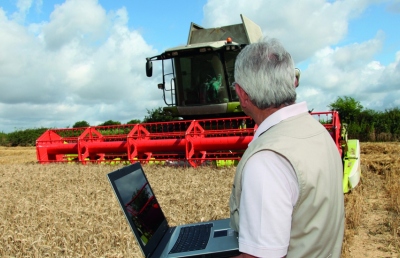 Man in field with laptop, next to a combine.