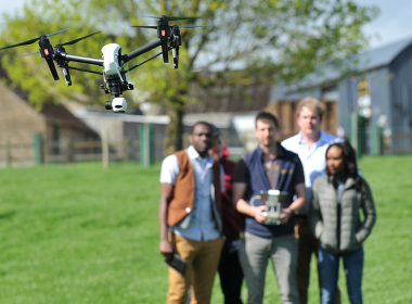 A group of four people in a field, one of whom is flying a drone