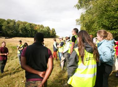 Delegates in a field listening to a farmer standing in front of herd of cows