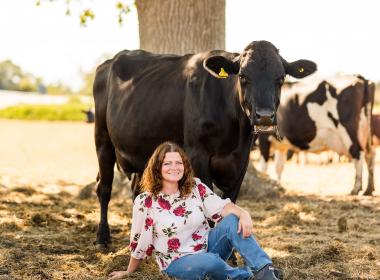 Woman seated next to standing cow